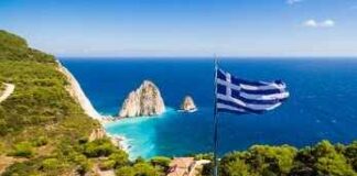 Greek flag overlooking a coastal cliff and turquoise sea