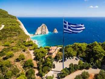 Greek flag overlooking a coastal cliff and turquoise sea