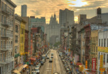 A bustling street in Chinatown, New York City, with historic buildings and vehicles under a sunset sky