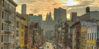 A bustling street in Chinatown, New York City, with historic buildings and vehicles under a sunset sky
