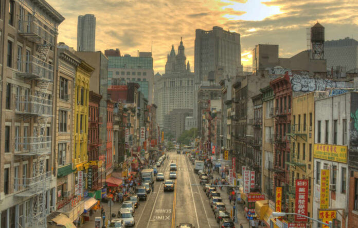 A bustling street in Chinatown, New York City, with historic buildings and vehicles under a sunset sky