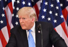 Trump’s Underground Fortress Sparks Billion-Dollar Fight A man in a suit speaking at a podium with American flags in the background