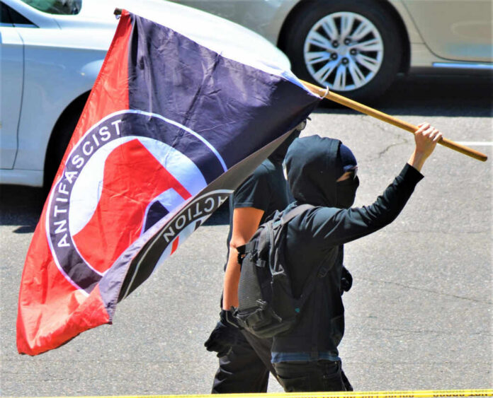 shutterstock_1472772557 Individual holding an antifascist flag during a protest