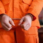 Guilty Plea Ends Years Of Questions A person in an orange jumpsuit with handcuffs