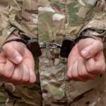 Person in military uniform with hands cuffed together
