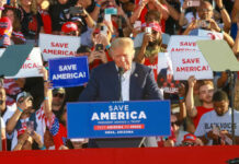 Donald Trump speaking at a political rally with supporters holding signs