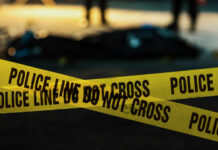 Decapitated Teen Finally Named — 26 Years Late Yellow police caution tape at a crime scene with blurred figures in the background