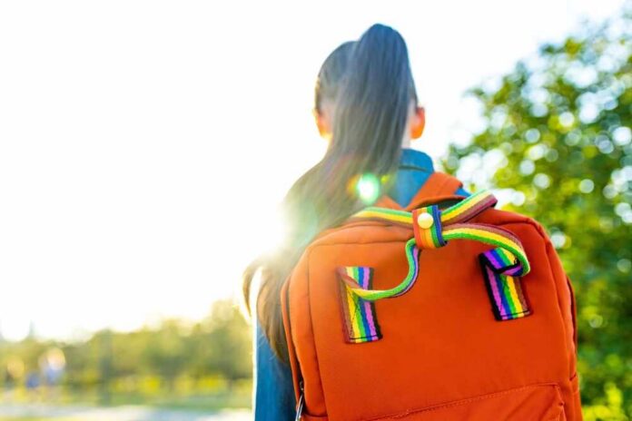 A young person with a colorful backpack standing in sunlight