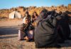 A young girl in traditional clothing sitting among a group of women in a refugee camp
