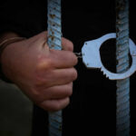A hand holding handcuffs attached to prison bars