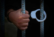 A hand holding handcuffs attached to prison bars