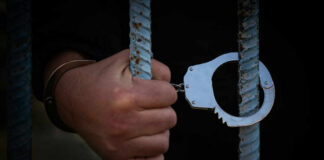 A hand holding handcuffs attached to prison bars
