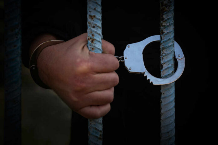 A hand holding handcuffs attached to prison bars