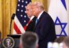 Spy Wars Erupt Inside Washington’s Inner Circle Donald Trump and another official at a press conference with flags in the background