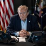 High Court Reshapes Presidential Authority A serious-looking man seated at a table with phones and an American flag in the background