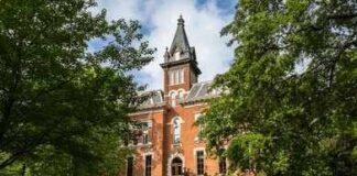 Students walking past a historic stone archway and ornate gate on a university campus