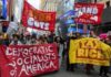 Protesters march in a city with large red banners