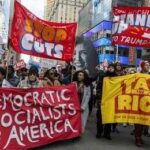 Protesters march in a city with large red banners