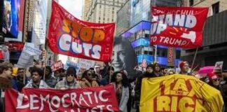 Protesters march in a city with large red banners