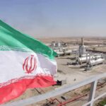 Iran Rejects Cease-Fire As Tensions Soar Iran flag over an oil and gas facility in a desert landscape