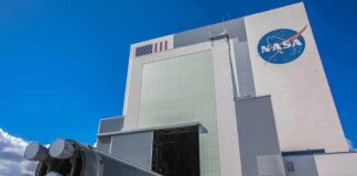 Rocket stage moved on transporter outside large NASA assembly building