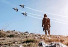 Soldier standing on rocky hillside watching fighter jets fly overhead