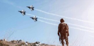 Soldier standing on rocky hillside watching fighter jets fly overhead