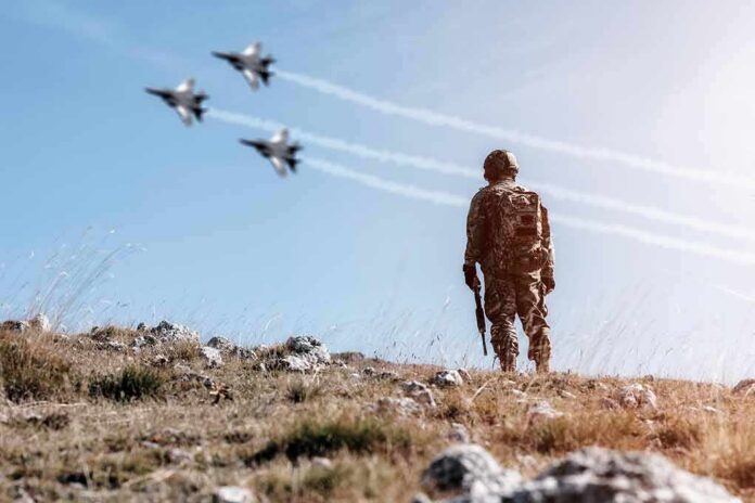 Soldier standing on rocky hillside watching fighter jets fly overhead