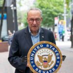 Genocide Claim Hijacks Schumer’s Big Reveal man speaking at a podium with a United States Senate seal