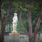 Stone statue of a woman in a cemetery framed by tree trunks