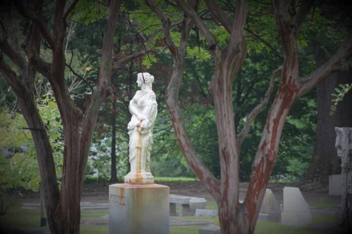 Cemetery,In,Memphis,Tennessee-,Elmwood Stone statue of a woman in a cemetery framed by tree trunks