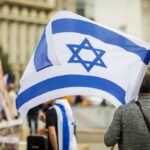 U.S. Aid Exposed — Who Really Backs Israel? Person holding an Israeli flag at a public demonstration