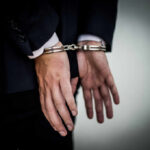 A person in a suit with hands cuffed behind their back