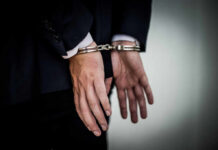 Fugitive Doctor Captured After Two Decades A person in a suit with hands cuffed behind their back
