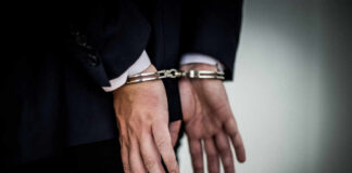 A person in a suit with hands cuffed behind their back