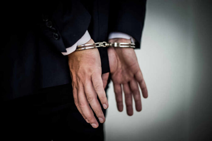 Businessman,Arrested,With,Handcuffs,On,Back,For,Corruption,And,Stealing A person in a suit with hands cuffed behind their back