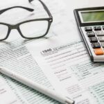 Tax forms with calculator, glasses, and pen
