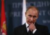 Putin Stages Normalcy Amid War man in suit at podium touching his face