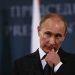 man in suit at podium touching his face