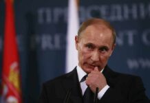 Putin Stages Normalcy Amid War man in suit at podium touching his face