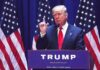 man in suit speaking at podium with multiple American flags