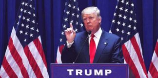 man in suit speaking at podium with multiple American flags