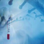 Gloved hand holding a COVID-19 test tube beside a stylized DNA helix
