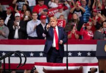 Massive Rally, Bigger Gamble For Trump man in suit points from a stage at a political rally