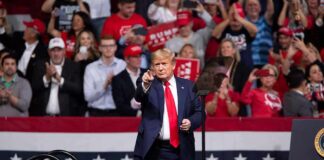 man in suit points from a stage at a political rally