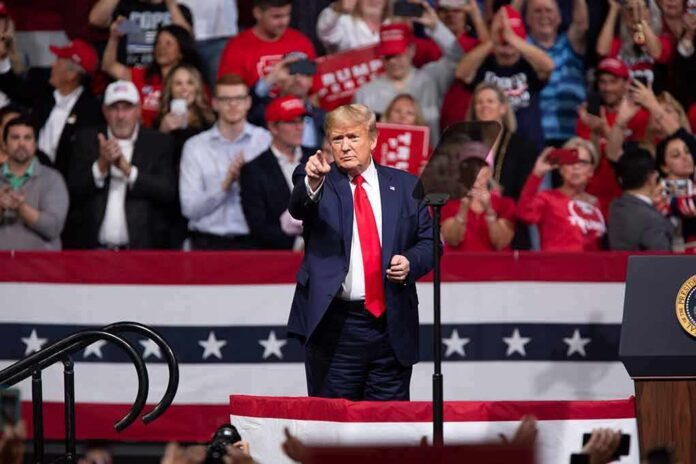 man in suit points from a stage at a political rally