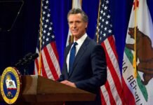 Transparency Flip-Flop: Where Are Newsom’s Taxes? Man in suit speaking at a podium with American and California flags