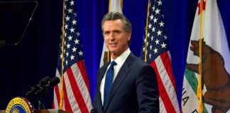 Man in suit speaking at a podium with American and California flags