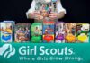 Girl Scout displays assorted cookie boxes on a table