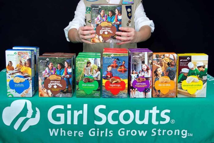 Girl Scout displays assorted cookie boxes on a table